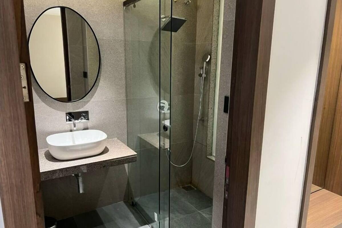 Een moderne badkamer met een ronde spiegel, een witte wastafel en een douchecabine met glazen wanden.