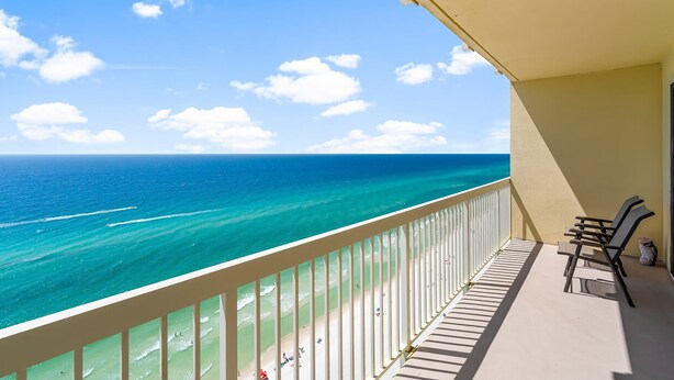 A balcony with a view of the ocean, a white railing, and a chair.