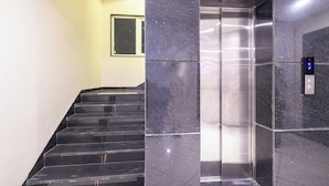 Ein moderner Aufzug mit digitaler Anzeige neben einer Treppe mit schwarzen Marmorstufen und -wänden.