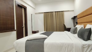 Ein Hotelzimmer mit Bett, einer Holztür, einem Spiegel, einem Fenster mit Vorhängen und einem Kopfteil.