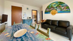 A living room with a dining table, a black leather sofa, and a kitchen in the background. - Bright Apartment Close to the Beach (Caorle)