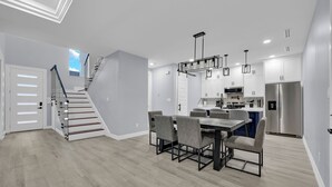 A modern kitchen with white cabinets, stainless steel appliances, and a dining area with a wooden table and chairs.