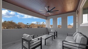 A spacious balcony with a ceiling fan, a sofa, two chairs, and a table.