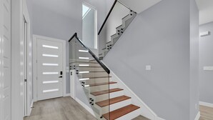 A modern staircase with glass railings and wooden steps, leading to a white door.