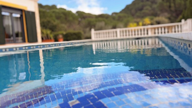 A swimming pool with tiled edges, a white fence, and a building with a yellow door in the background.