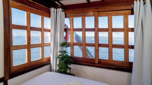Una habitación con una cama, un libro abierto y vista al mar a través de amplios ventanales.