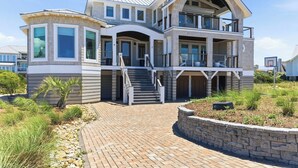 A multi-story house with a prominent balcony, a driveway, and a stone retaining wall.