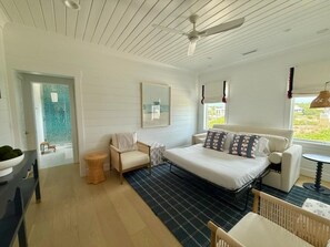 A bedroom with a bed, a chair, a small table, a window with a view, and a ceiling fan. - New Ocean Front Luxury Award Winner 6 BR 6.5 BA BHI and Shoals A Rare Find (Bald Head Island)