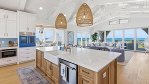 A modern kitchen with a large island, white cabinetry, and a view of the ocean.