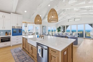 Una cocina moderna con una isla grande, armarios blancos y vistas al océano.