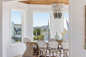 A dining area with wicker chairs, a wooden table, and a decorative chandelier.