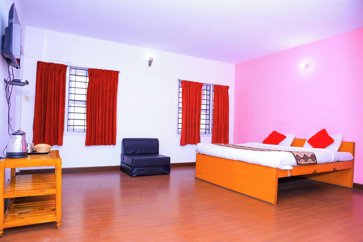 A room with a bed, a chair, a table, and two windows with red curtains.
