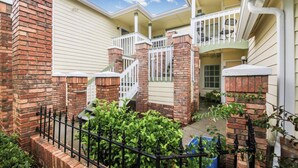 A two-story house with a brick exterior, a white porch with a railing, and a small garden area.