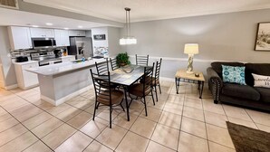 A modern kitchen with a central island, dining area with chairs, a sofa, and a lamp.