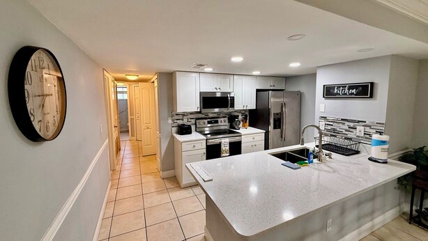A modern kitchen with white cabinets, stainless steel appliances, a large island, and a clock on the wall.