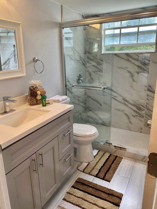 Un baño moderno con ducha envuelta en vidrio, un salpicadero de mármol y un tocador con lavabo y espejo.