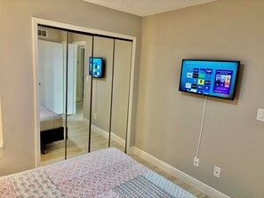 A bedroom with a bed, a TV mounted on the wall, and a sliding door closet.