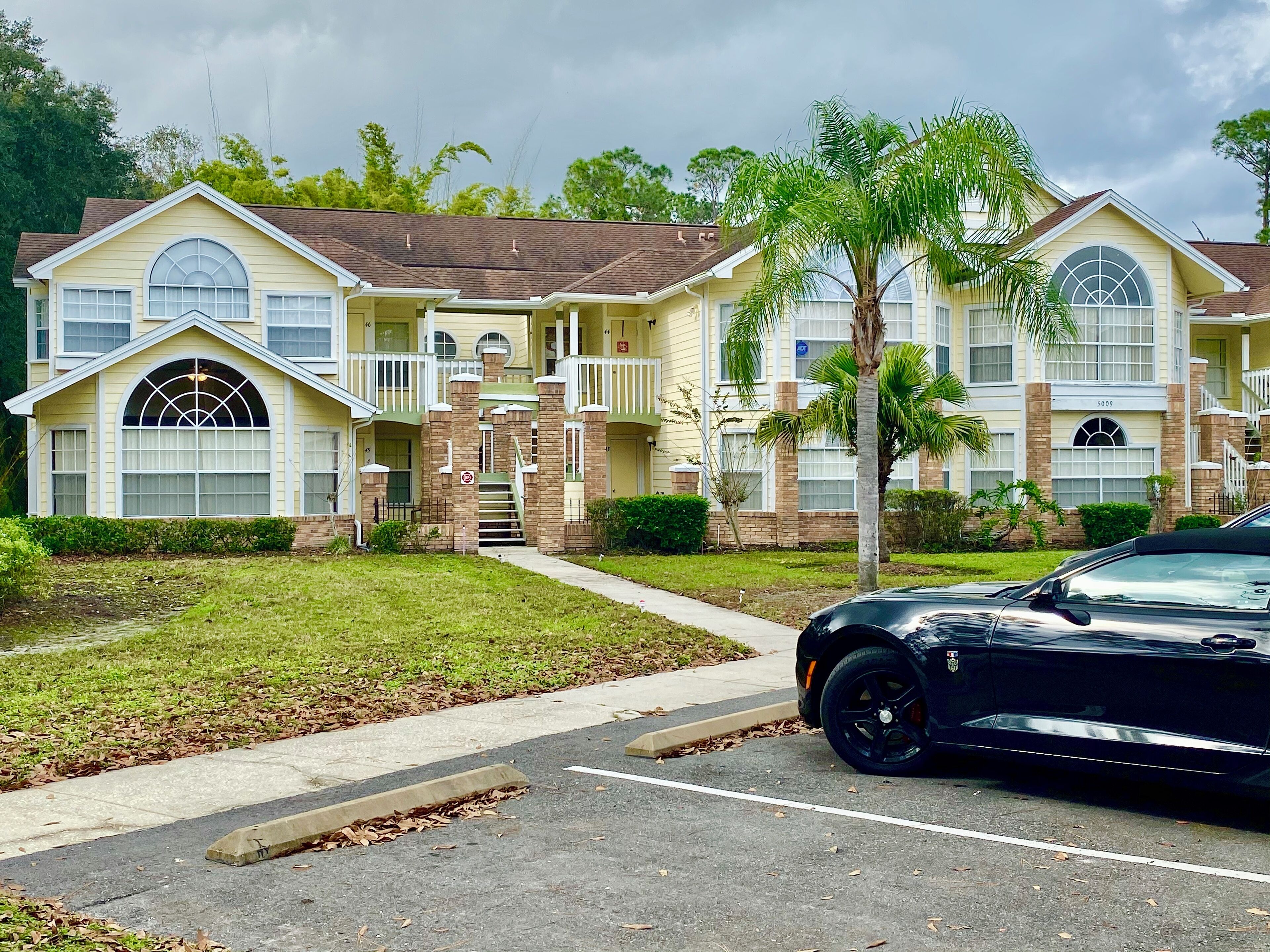 A two-story building with a central entrance, a covered porch, and a parking lot with a black car.