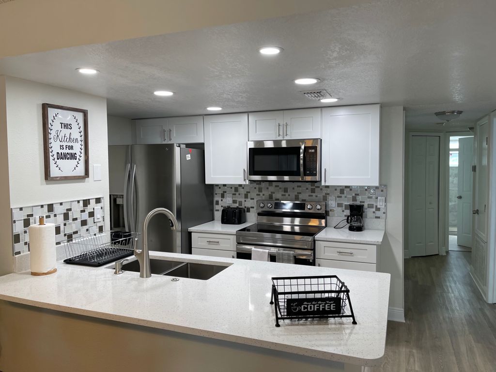 A modern kitchen with white cabinets, stainless steel appliances, and a coffee station.