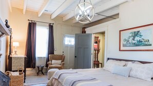 A cozy bedroom with a large bed, a chair, a small table, and a door leading to another room. - c1815, 3-bedroom Bed & breakfast in charming Historic Brownsburg with WiFi, AC (Rockbridge Baths)