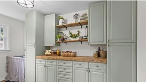 A kitchen with light green cabinets, wooden shelves, and a countertop with various items.