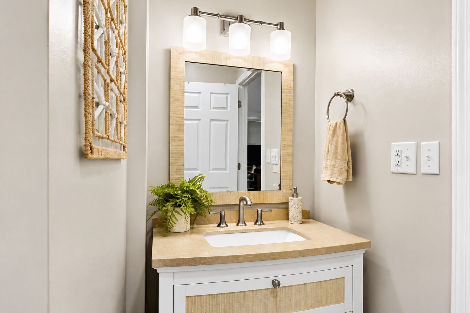 A bathroom with a large mirror, three light fixtures, a sink, a towel rack, and a potted plant.