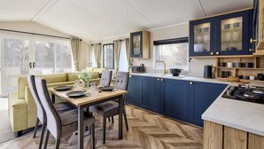 A modern kitchen with dark blue cabinets, a herringbone wood floor, and a dining area with a green sofa and wooden table.