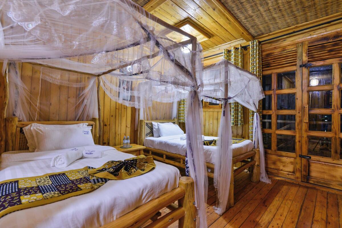 Eine Holzhütte mit zwei Betten, jedes mit Baldachin, und einem kleinen Tisch dazwischen.