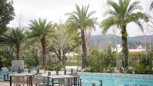 A pool area with a table and chairs, surrounded by palm trees and a mountain view. - Feeling Hotel (Beinan)