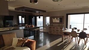 Un salon moderne comprenant un canapé, une table basse et un coin repas avec une table et des chaises. Il y a également une cuisine avec un comptoir et une vue sur la mer.