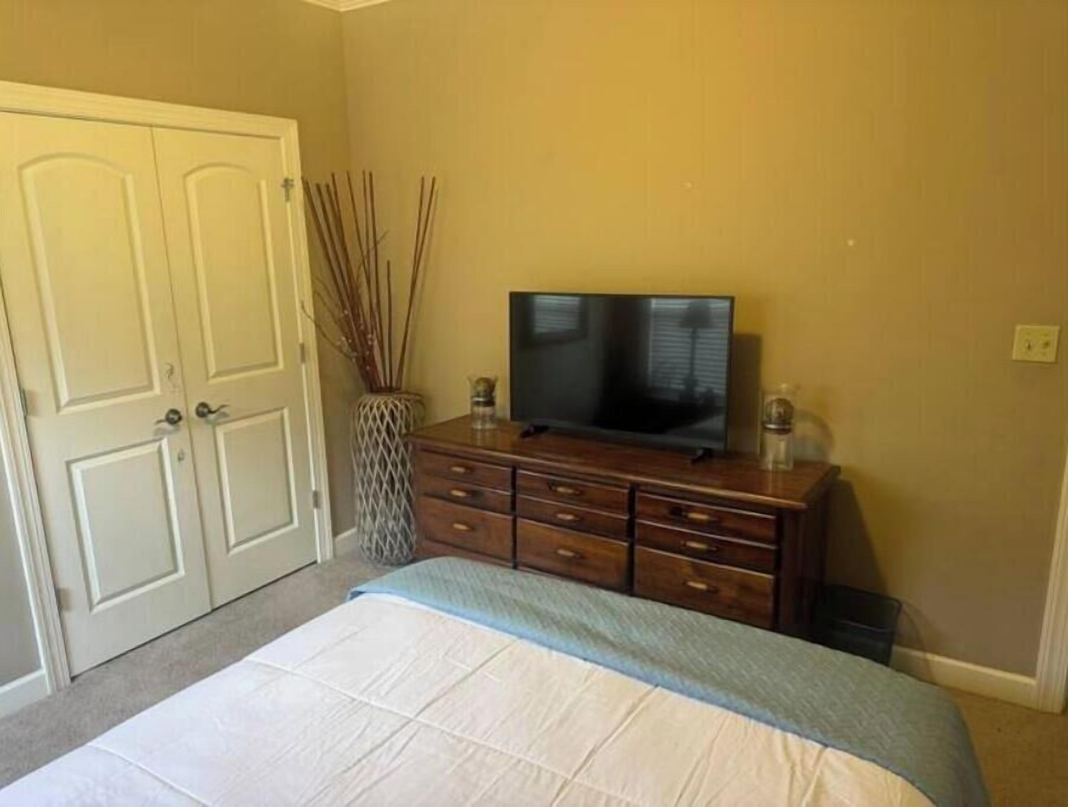 Un dormitorio con cama, cómoda, televisor y puerta.