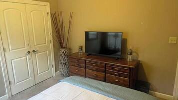 Un dormitorio con cama, cómoda, televisor y puerta.