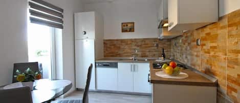 A modern kitchen with white cabinets, a wooden backsplash, and a dining area with a table and chairs.