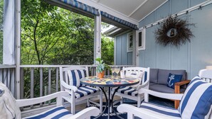A covered porch with white and blue striped chairs, a round table with a colorful tablecloth, and a gray sofa. - (3 Nt Summer Min!) Union Pier Condo With Heated Pool! July 04-10 OPEN! (Union Pier)