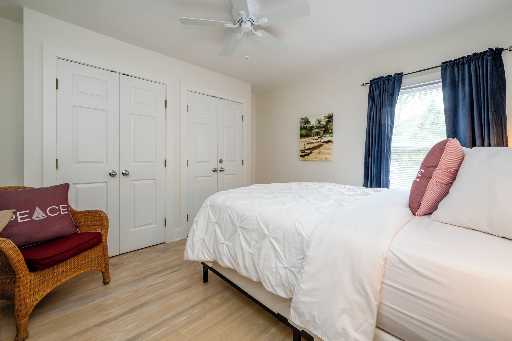 A bedroom with a bed, a chair, a ceiling fan, and a painting on the wall.