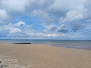 Una playa con una amplia orilla arenosa y un mar tranquilo bajo un cielo parcialmente nublado.
