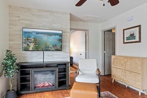 A living room with a fireplace, a television mounted on a wall, a white chair, and a wooden cabinet. - Waterfront Home - Hot Tub, Dock, Fire Pit, Boat (Lake Norman of Catawba)