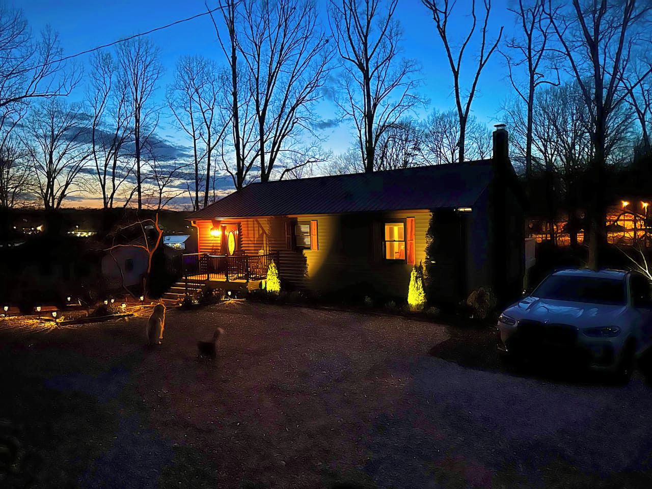 A house with a gravel driveway, a car parked in front, and a dog in the foreground.