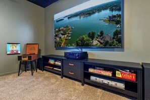 Una sala de entretenimiento con un televisor de pantalla plana grande montado en la pared, un mueble de madera con cajones y piso alfombrado.