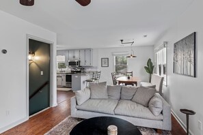 Una sala de estar moderna con un sofá gris, una mesa de comedor y una cocina al fondo.