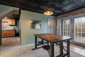 A dining area with a wooden table and chairs, a pendant light, and a view of a kitchen and a door with frosted glass panels. - Waterfront Home - Hot Tub, Dock, Fire Pit, Boat (Lake Norman of Catawba)