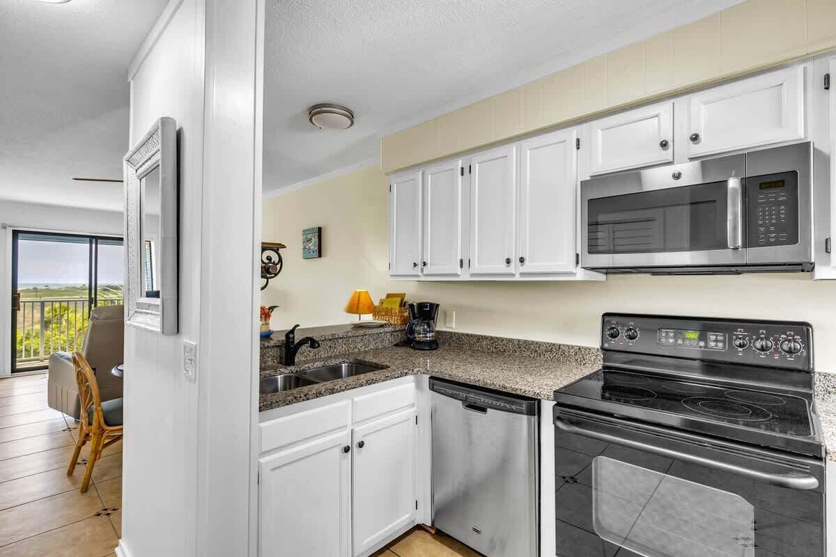 Una cocina con gabinetes blancos, microondas, estufa y lavavajillas.