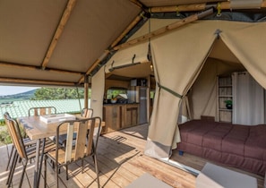 Un hébergement sous tente comprenant une table à manger, des chaises, un lit et un coin cuisine.