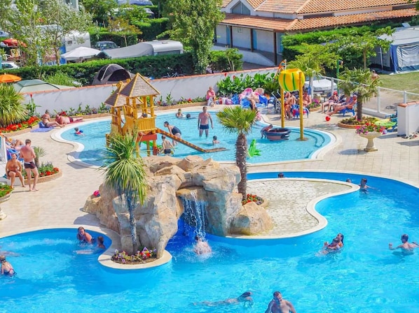 Une grande piscine extérieure dotée de nombreux éléments aquatiques, notamment une cascade et un espace de jeux.