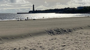 Una playa con un faro al fondo, orilla arenosa y cielo despejado.