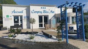Un edificio con letreros que dicen "Accueil" y "Camping Bleu Noir", una banca y una estructura de pérgola azul.