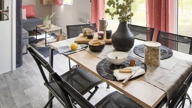 Een eetgedeelte met een tafel gedekt voor twee personen, een vaas met bloemen en een raam met gordijnen.