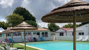 Zwembad met witte ligbedden en rieten parasols, omringd door een wit gebouw met een rood dak.