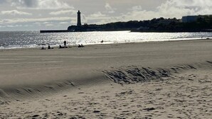 Een strand met een vuurtoren op de achtergrond, zandstrand en heldere lucht.