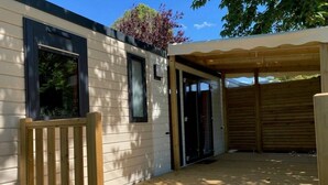 Een houten terras met een overdekte patio, een houten stoel en een gebouw met grote ramen en een deur.